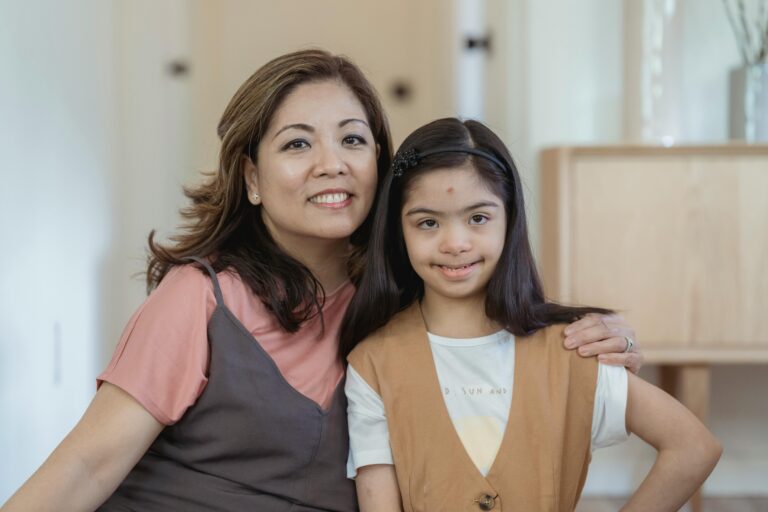 A mother and daughter with Down syndrome embracing and smiling indoors.